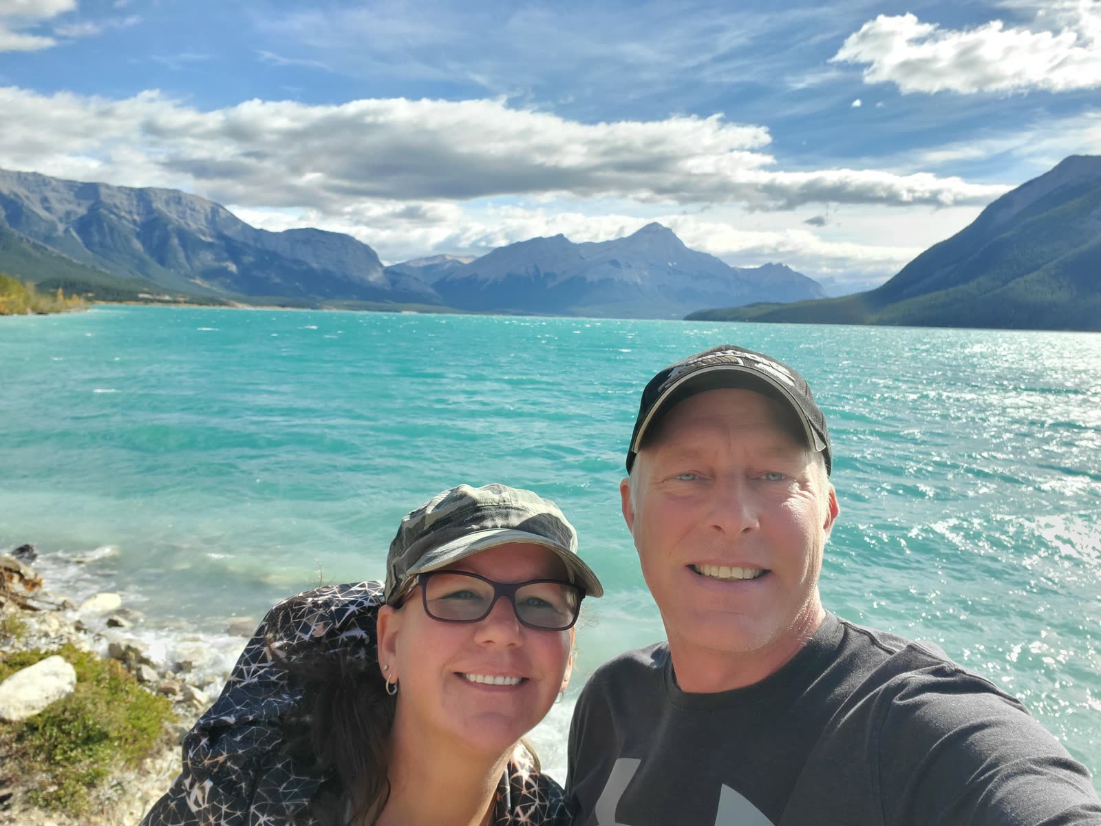 Derek and Michelle smiling in front of a turquoise mountain lake